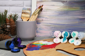 Artist's palette, tubes of colorful paint, brushes and canvas with abstract painting on textured...