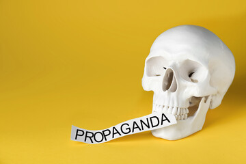 Information warfare concept. Human skull and paper card with word Propaganda on yellow background,...
