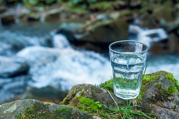 Glass of fresh water on stone with moss near stream. Space for text