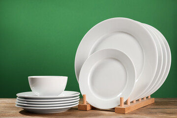 Set of clean dishware on wooden table against green background