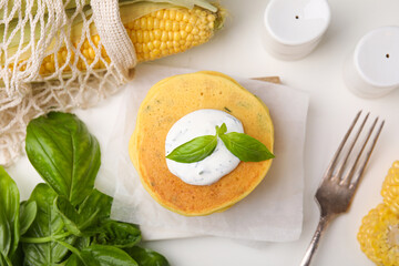 Tasty corn pancakes with sauce and basil leaves served on white table, flat lay