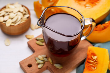 Fresh pumpkin seed oil in glass pitcher on white wooden table
