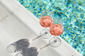 Glasses of tasty rose wine on swimming pool edge, space for text - obrazy, fototapety, plakaty
