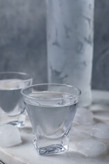 Shot glasses and bottle of vodka with ice cubes on table
