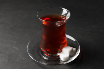 Glass with traditional Turkish tea and sugar cubes on black table, closeup
