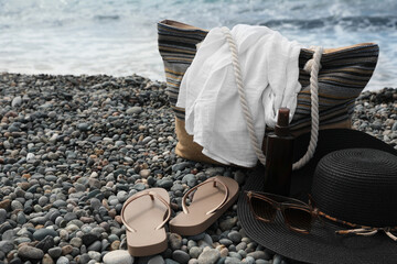 Beautiful hat with sunglasses, bag and flip flops near sea on pebble beach