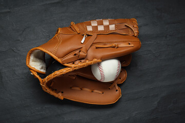 Catcher's mitt and baseball ball on black slate background, top view. Sports game