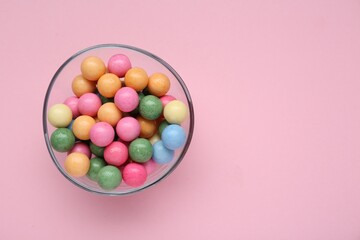Bowl with many bright gumballs on pink background, top view. Space for text