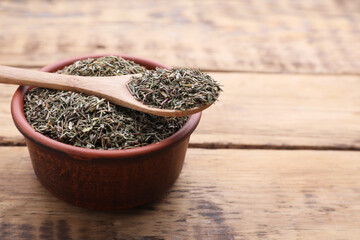 Bowl and spoon with dried thyme on wooden table, closeup. Space for text