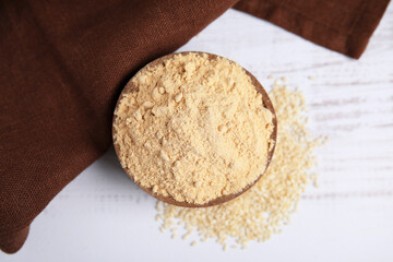 Sesame flour in bowl on white wooden table, top view