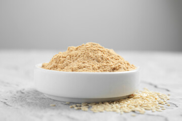 Sesame flour in ceramic bowl on white textured table, closeup