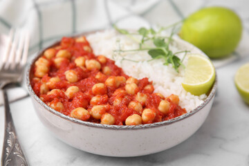 Delicious chickpea curry with rice in bowl on white marble table, closeup