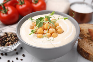 Tasty chickpea soup in bowl on white tiled table, closeup