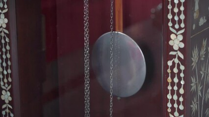 Close-up of an antique grandfather clock's shiny pendulum swinging back and forth. The clock pendulum moves to the rhythm of the music, evoking a feeling of nostalgia.