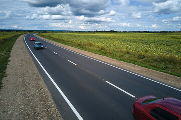 Aerial view of intercity road between green agricultural fields with fast driving cars. Top view...