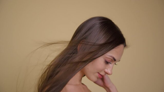 Slow motion of the flying hair of a cute brunette girl. Yellow background.