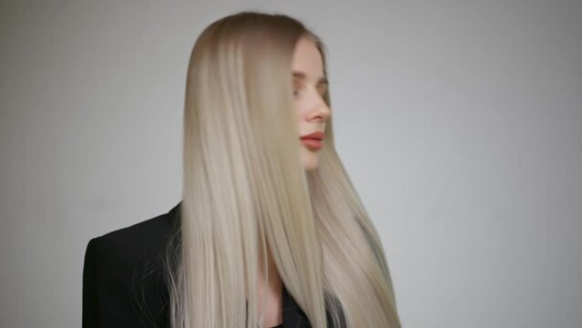 Slow motion of the long hair of a charming blonde. Grey background.