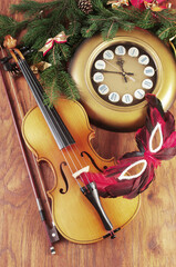 Violin, wall clock, carnival mask and Christmas decorations on wooden texture.