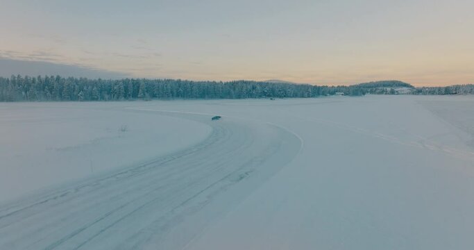 Aerial view chasing Norbotten driver drifting corners on frozen Lapland ice lake at sunrise