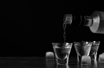 Pouring vodka from bottle in glass and ice cubes on grey table. Space for text - obrazy, fototapety, plakaty
