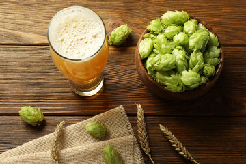 Glass of beer, fresh green hops and spikes on wooden table, above view