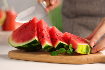 Woman cutting delicious watermelon at white wooden table indoors, closeup