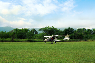 Fototapeta na wymiar Light aircraft on grass near trees and mountains