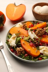 Delicious persimmon salad with cheese and pomegranate served on white table, closeup