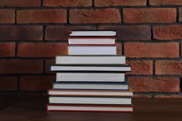 Stack of hardcover books on wooden table near brick wall