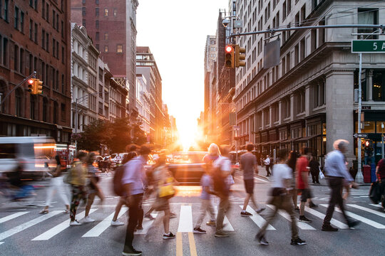 Diverse crowds of people walking through a busy intersection on 5th Avenue and 23rd Street in New York City with sunset background
