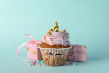 Cute sweet unicorn cupcake and gift boxes on light turquoise background