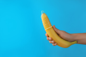 Woman holding banana in condom on light blue background, closeup and space for text. Safe sex...