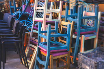 Fototapeta na wymiar Chairs piled up in empty cafe, the end of touristic season, closed restaurant in the european streets, bad season, end of working hours, seats stacked in after hours, restaurant went bust bankrupt
