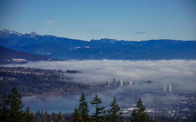 Cloud inversion over buildings at Port Moody, BC, near mist-covered Burrard Inlet, with mountain backdrop.
