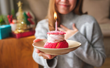 Closeup image of a surprised young woman receiving and holding birthday cake with candle, Christmas holiday decoration at home