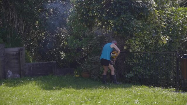 An Old Man Cutting Grass Using A Manual Grass Cutter At The Backyard. Tracking Shot