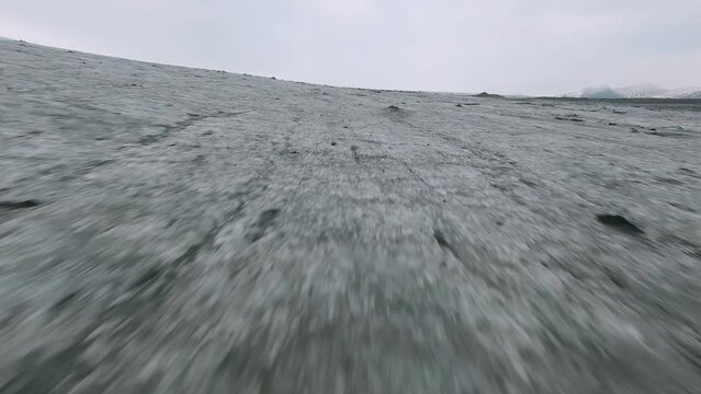 FPV drone shot over a thin layer of dirty ice on a melting Glacier in cloudy Iceland