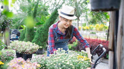 Gardening blossom and Asian woman people concept - happy smiling Adult female in apron with flower  care fertilizer at summer garden. Agriculture florist smiling activity happy hobby 