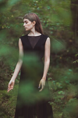 beautiful girl in the forest A young woman in a black dress balancing barefoot in the forest on covered with moss. Forest therapy concept.