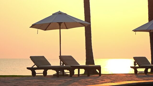 Close-up of empty beach loungers and sun umbrella at sunset.