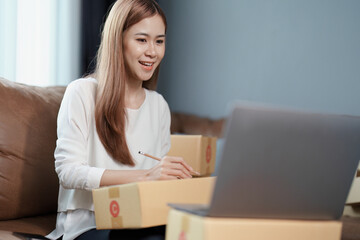 Starting small business entrepreneur of independent young Asian woman online seller is using computer and taking orders to pack products for delivery to customers. SME delivery concept