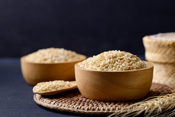 Fototapeta na wymiar Organic Thai brown rice grain in wooden bowl on black background, Asian healthy food ingredients