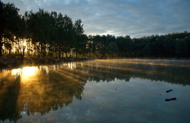 Naklejka premium Morning sun rays on the water of a small lake. Moscow region. Russia