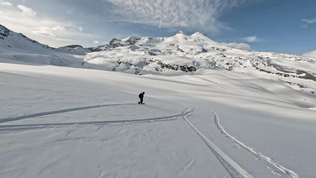 Aerial follow view extreme man snowboard downhill freeride carving on snowy mountain freedom. FPV sport drone shot snowboarding speed ride danger fast action outdoor leisure activity hobby in 4k