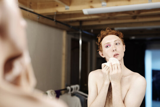 Young man standing in front of mirror removing his make up using cleansing wipes