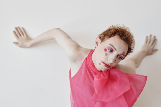 Horizontal fashion shot of young male model wearing pink outfit with unusual make-up posing on camera