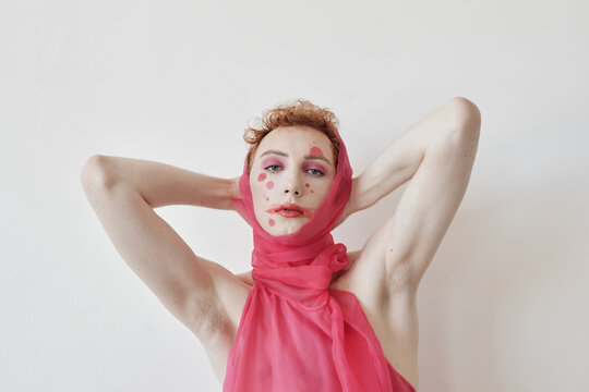 Fashion portrait of young man wearing pink outfit with clownlike make-up posing on camera