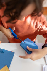 The child cuts colored paper with scissors at the table. the boy cuts a snowflake out of blue paper with scissors.