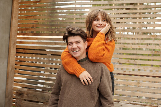 Young man and his attractive wife in stylish outfits posing on camera outdoors on porch