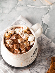 There is a white mug with hot chocolate and marshmallows on the marble light table. Copy space. Macro